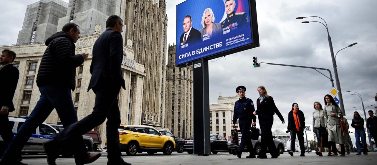 Menschen laufen im russischen Moskau an einer Tafel mit Wahlwerbung vorbei.