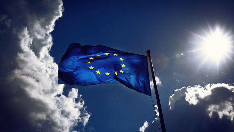 Eine EU-Flagge weht im Wind - im Hintergrund Himmel mitWolken und Sonne 