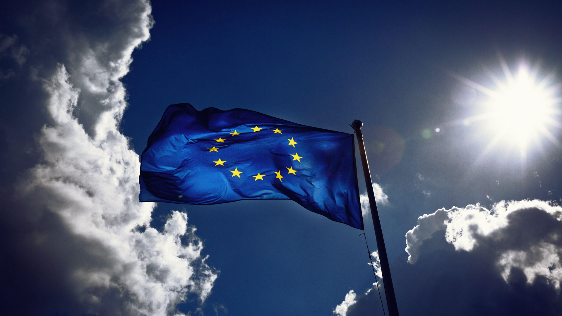 Eine EU-Flagge weht im Wind - im Hintergrund Himmel mitWolken und Sonne 