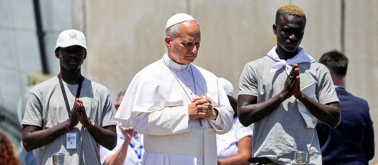 Papst Leo XIV. betet, neben ihm stehen die Migranten Musa und Pa. am Kai des Hafens von Arguineguín auf Gran Canaria, Spanien.