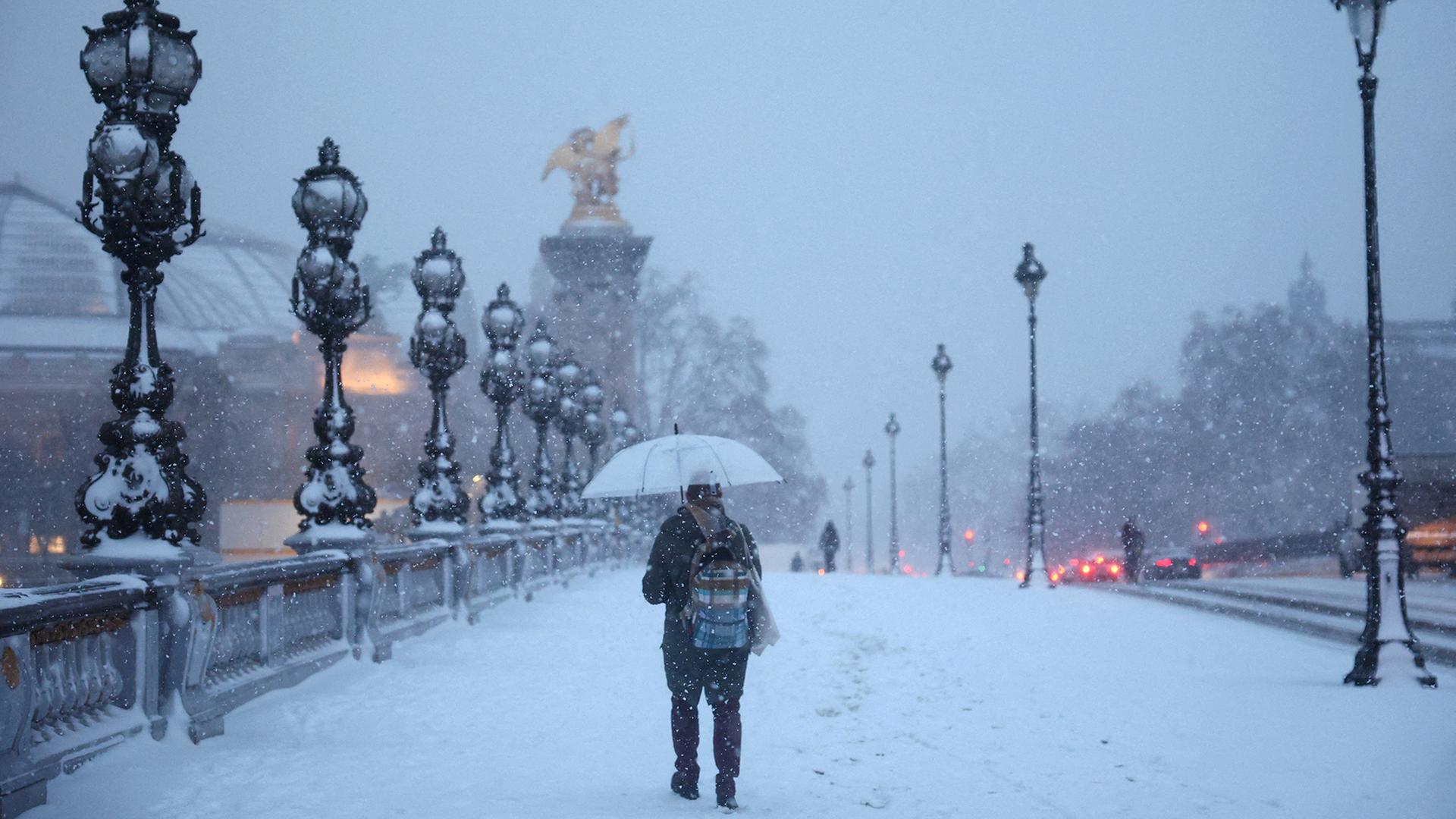 Eine Person schützt sich unter einem Regenschirm vor dem fallenden Schnee auf der schneebedeckten Alexandre-III-Brücke in Paris. | REUTERS