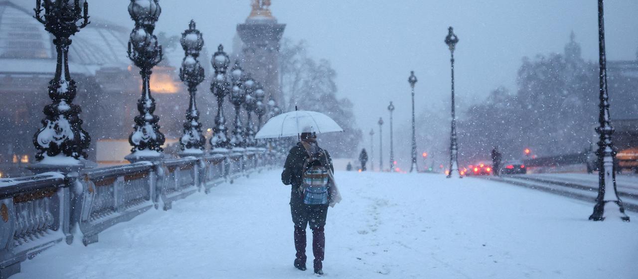 Eine Person schützt sich unter einem Regenschirm vor dem fallenden Schnee auf der schneebedeckten Alexandre-III-Brücke in Paris.
