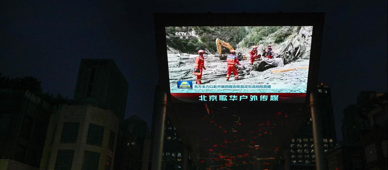 Auf einer Leinwand in Peking wird ein Beitrag gezeigt, der Bilder von Rettungskräften zeigt