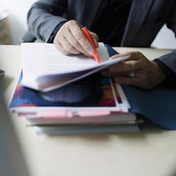 Akten auf einem Schreibtisch, vom Beamten sind nur die Ärmel des Sakkos zu sehen