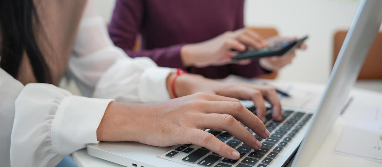 Zwei Personen an Laptop und Tablet in einem Büro.