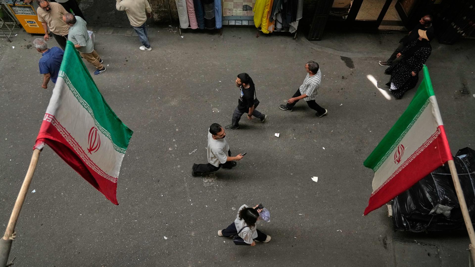In einem Basar in Teheran laufen Menschen unter iranischen Flaggen vorbei | AP