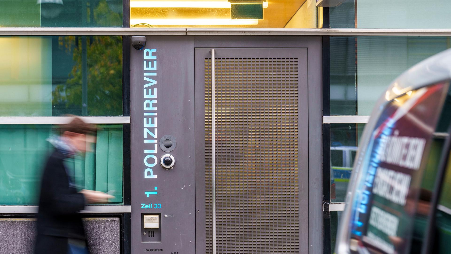 Ein Mann eilt, den Blick auf das Smartphone in seiner Hand gerichtet, an einer grauen Tür vorbei. Neben der Tür verläuft vertikal der Schriftzug: 1. Polizeirevier. | Andreas Arnold; picture-alliance/dpa