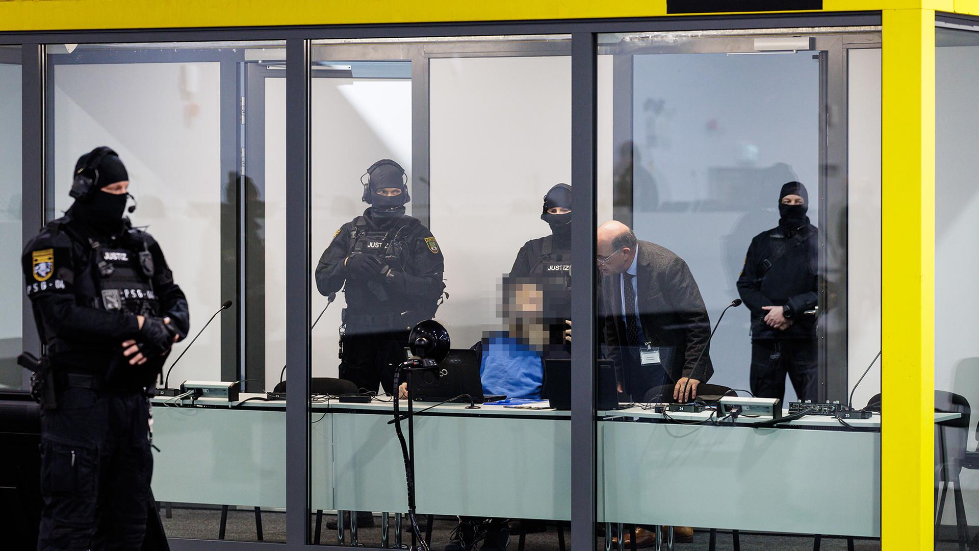 Ein Angeklagter sitzt von Polizisten bewacht hinter einer Glasscheibe. | EPA