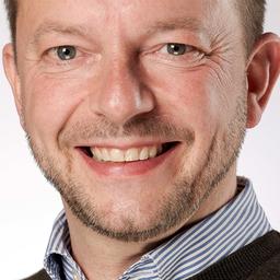 Mann mit kurzen braunen Haaren und kurzem Bart lächelt in die Kamera