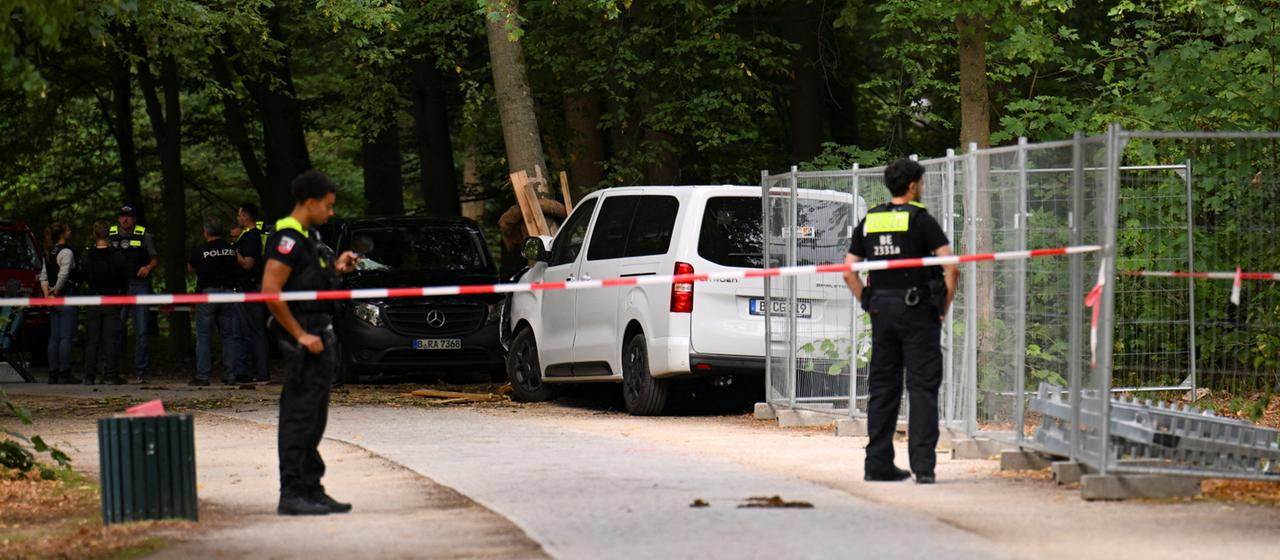 Polizisten stehen vor einem zerstörten weißen Fahrzeug im Bereich des Berliner Tiergartens