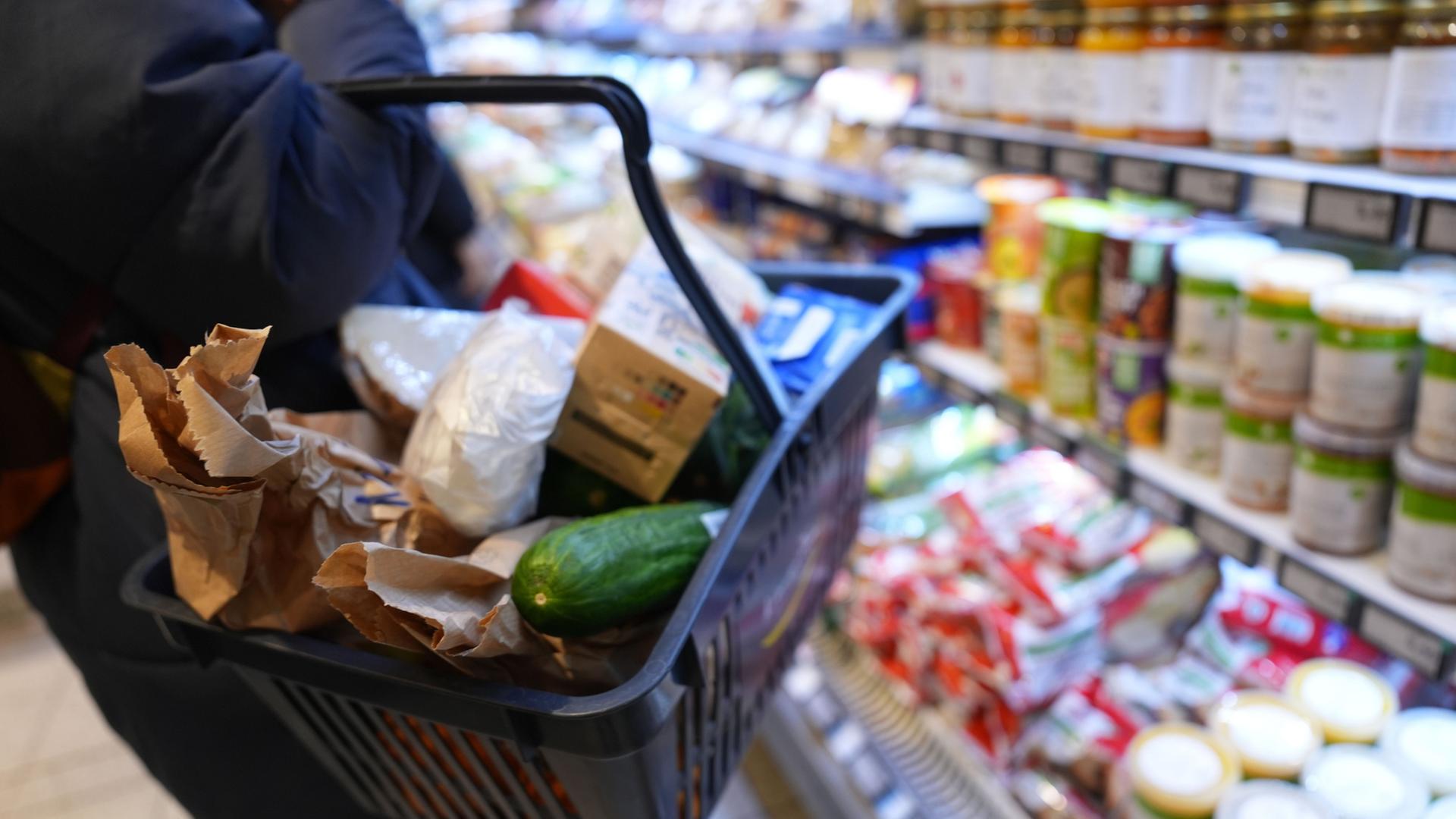 Eine Kundin geht mit einem Einkaufskorb und ihrem Einkauf an den Regalen in einem Supermarkt vorbei. | Marcus Brandt/dpa