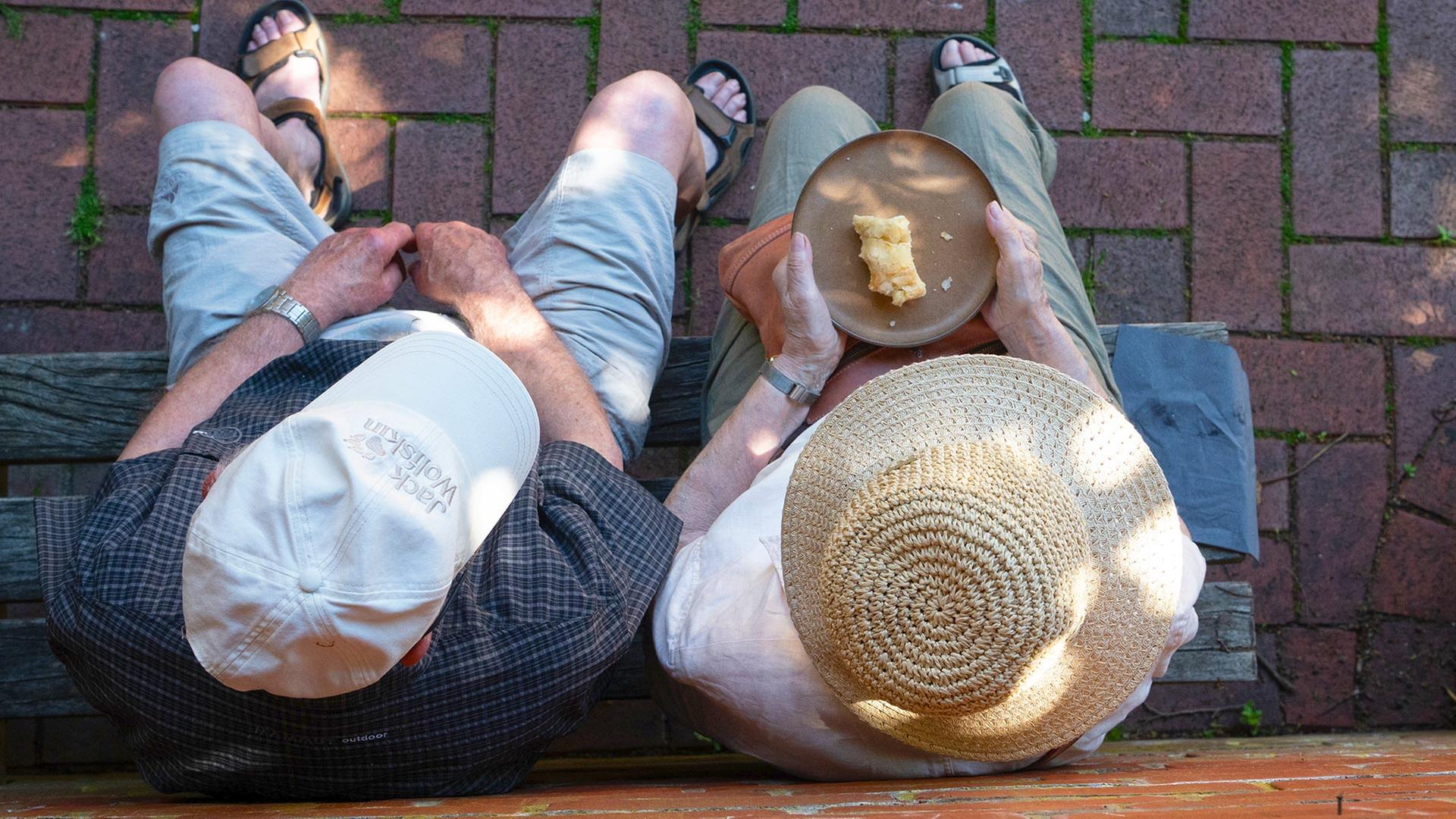 Zwei Senioren sitzen auf einer Bank und essen Kuchen. | picture alliance / SvenSimon