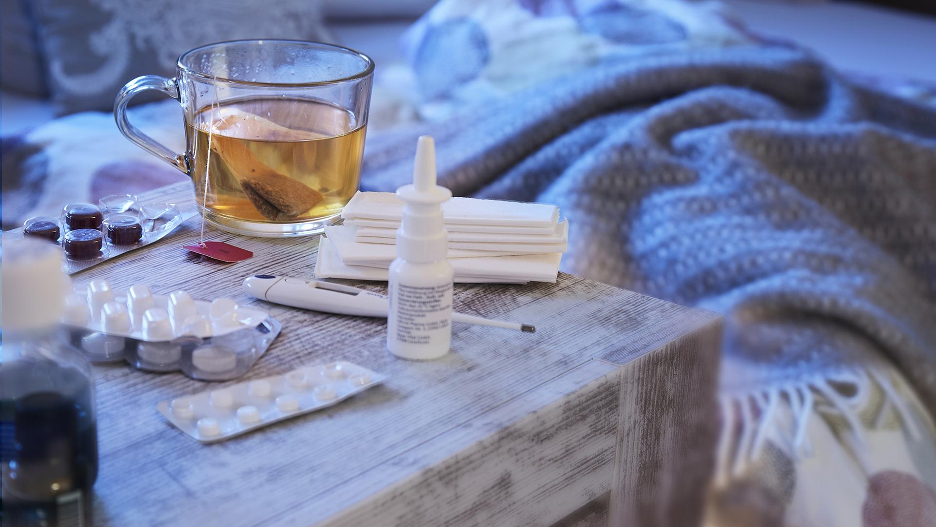 Tee, Nasenspray, Medikamente und ein Fieberthermometer auf einem Nachttisch. | ARD-aktuell