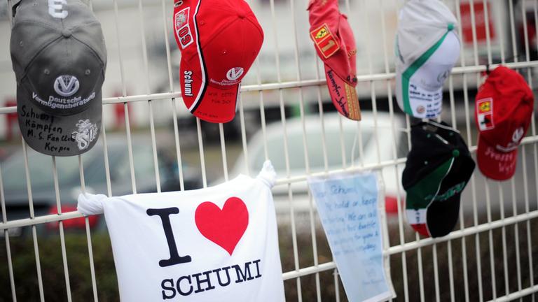 Mützen mit Aufschriften hängen nach Michael Schumachers Unfall an einem Zaun. 