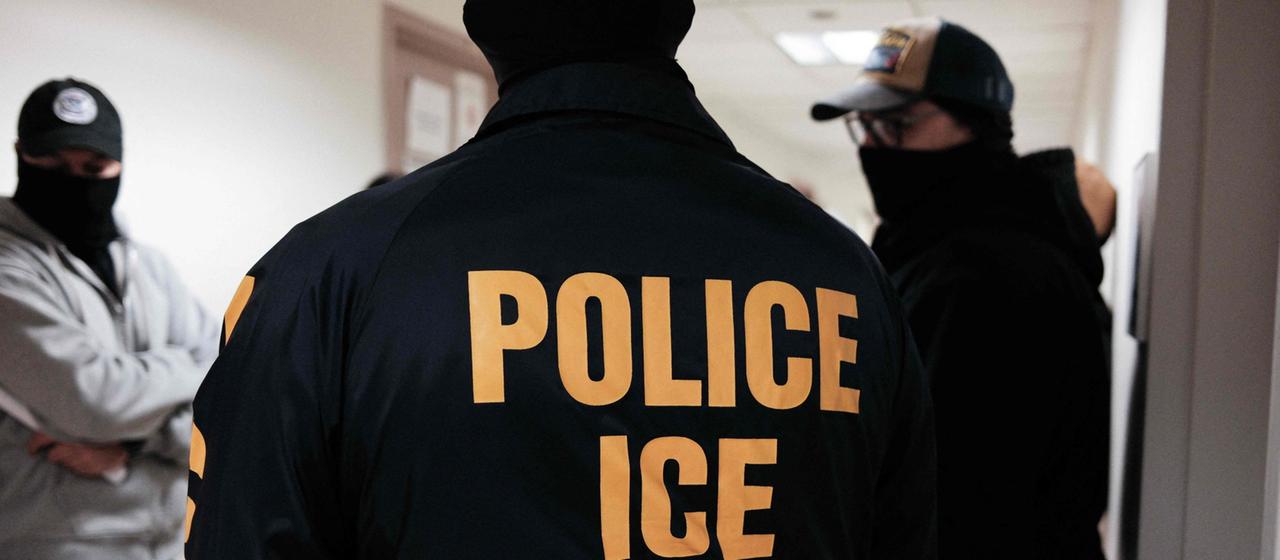 ICE-Einsatzkräfte stehen in einem Flur. 