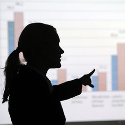 Frau steht vor einer an die Wand projizierten Grafik und erklärt sie