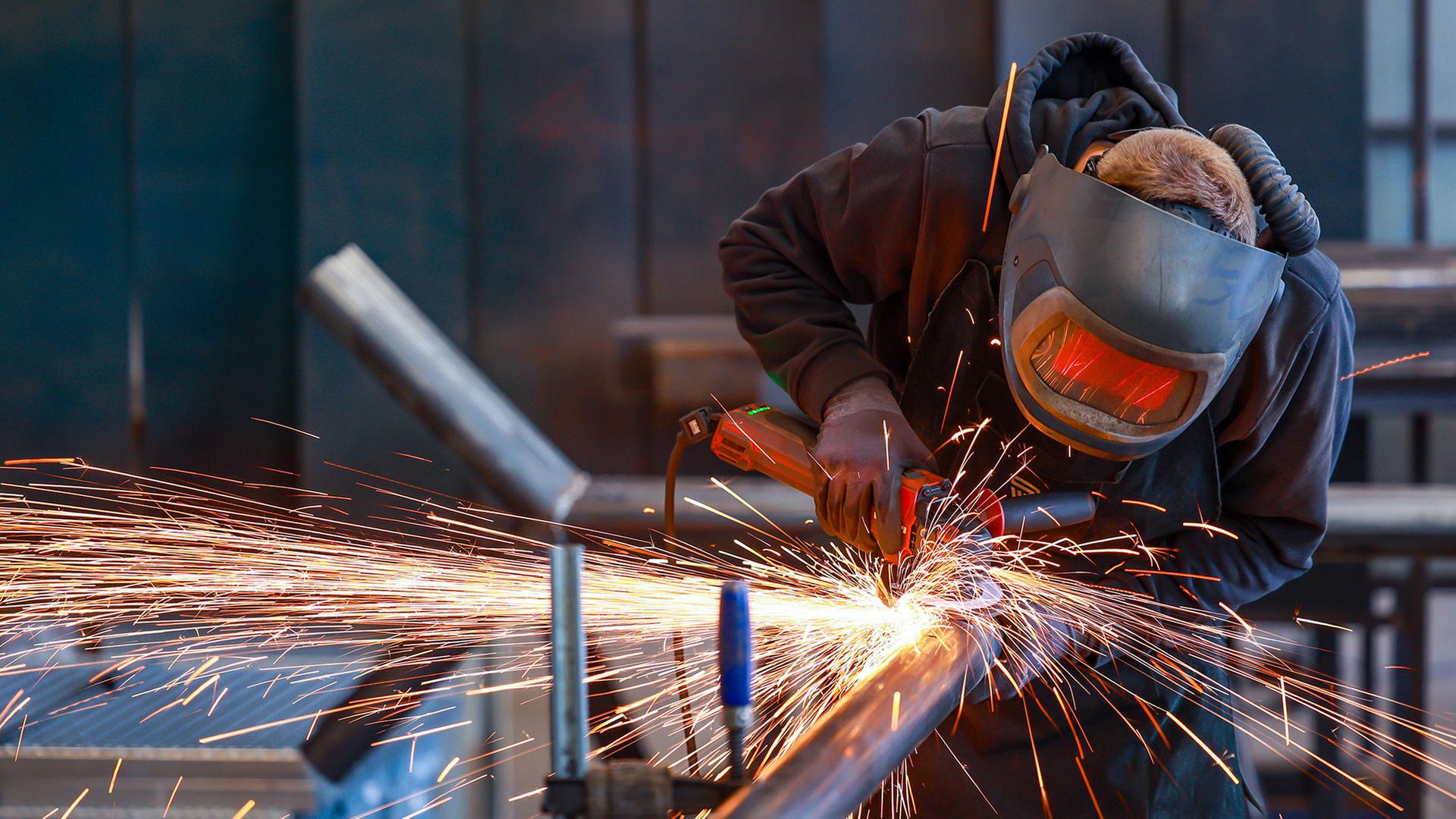 Ein Industriearbeiter flext mit einem Winkelschleifer ein Stahlrohr. | picture alliance / Rupert Oberh