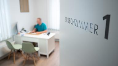 Ein Hausarzt sitzt in einem Sprechzimmer seiner Hausarztpraxis an einem Schreibtisch und arbeitet am Computer.