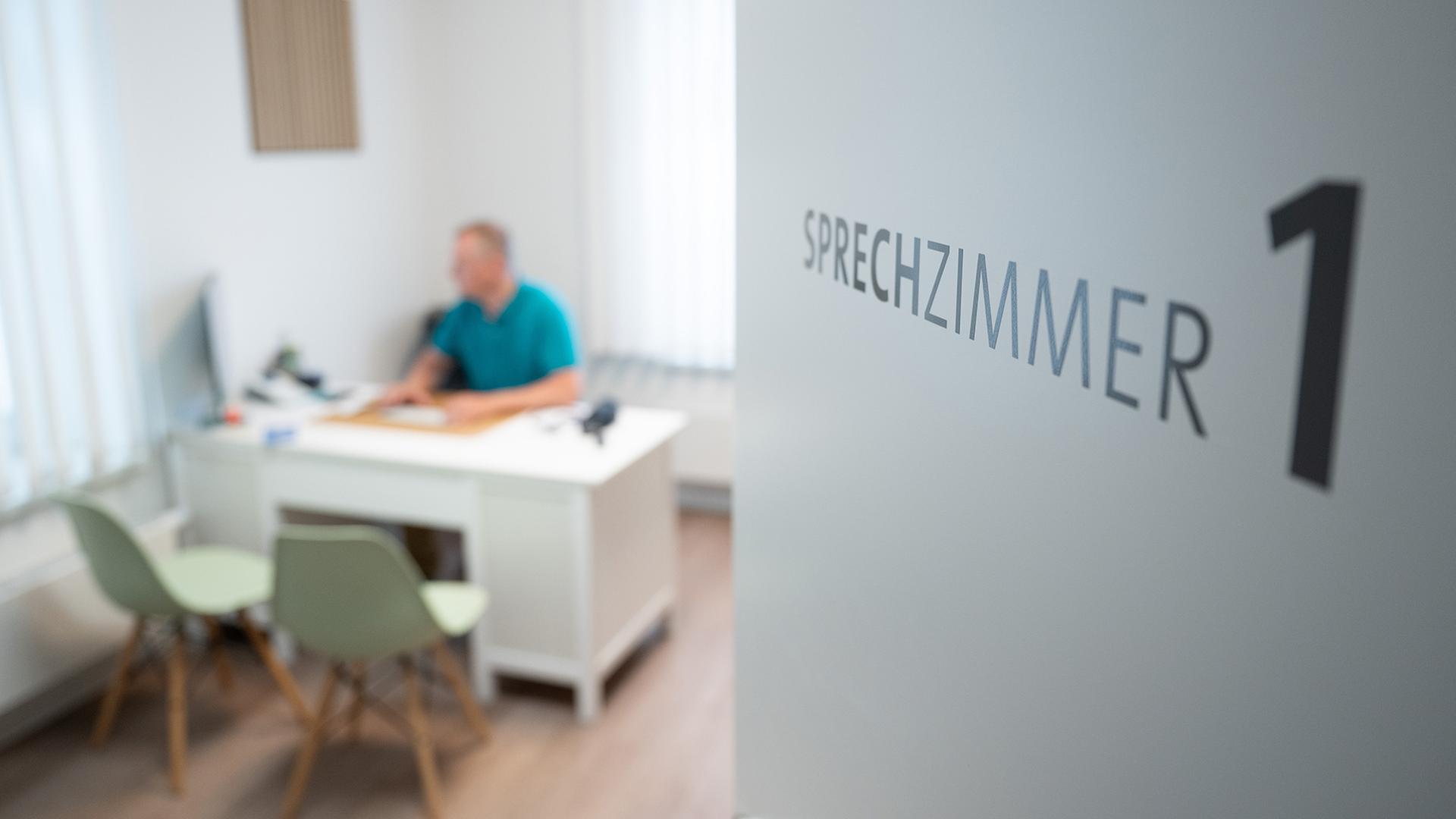 Ein Hausarzt sitzt in einem Sprechzimmer seiner Hausarztpraxis an einem Schreibtisch und arbeitet am Computer. | dpa