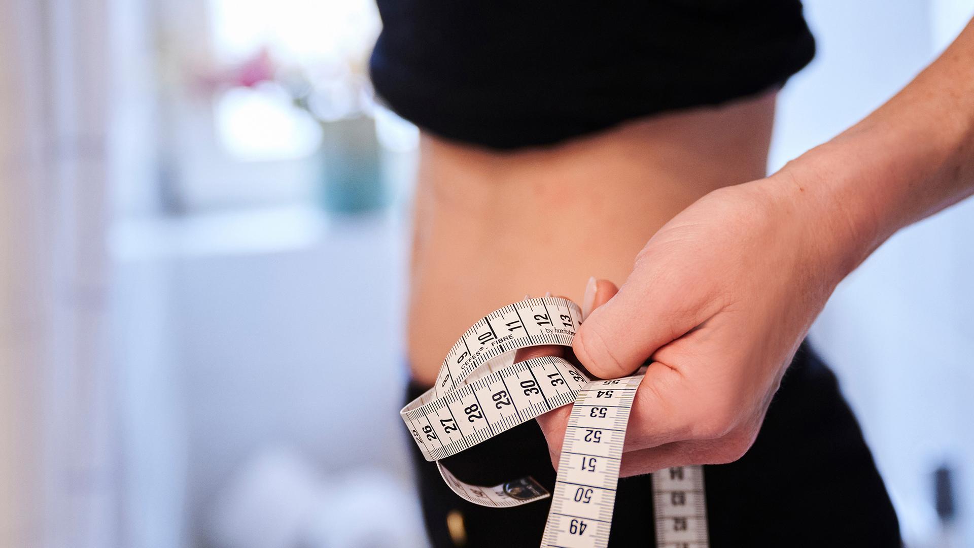 Eine Frau hält ein Zentimetermaßband an ihren Bauch. | dpa