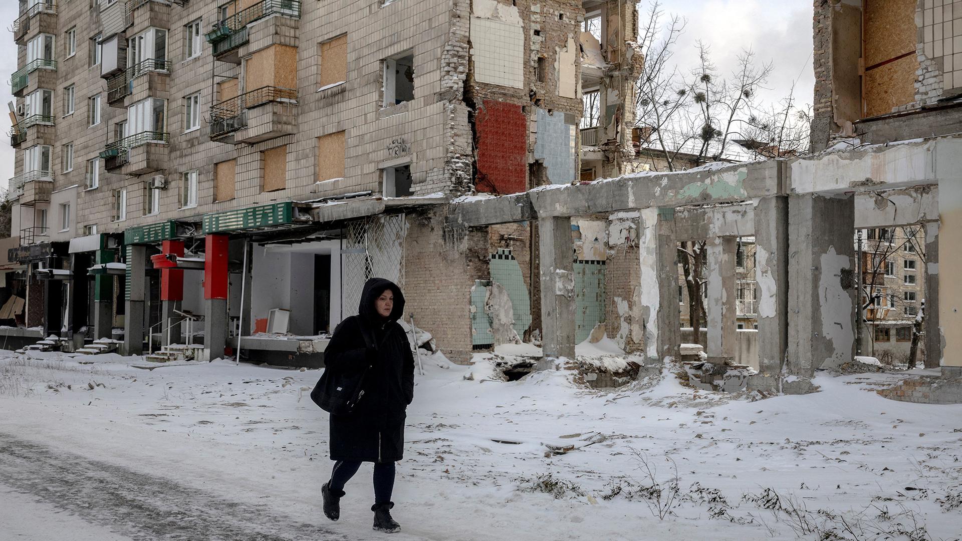 Eine Frau geht im Schnee an einem zerstörten Wohnhaus in Kiew vorbei. | REUTERS