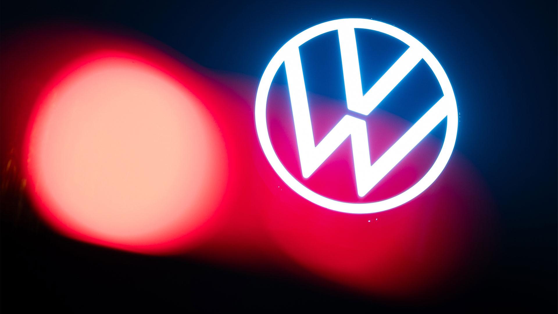 Eine Auto-Rückleuchte leuchtet vor dem Logo auf dem Dach des VW-Markenhochhaus | picture alliance/dpa
