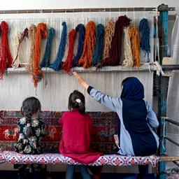 Rückenansicht dreier Mädchen, die in Kabul vor einem Webstuhl sitzen