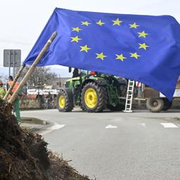 Eine EU-Flagge steckt in einem Misthaufen, dahinter steht ein Traktor