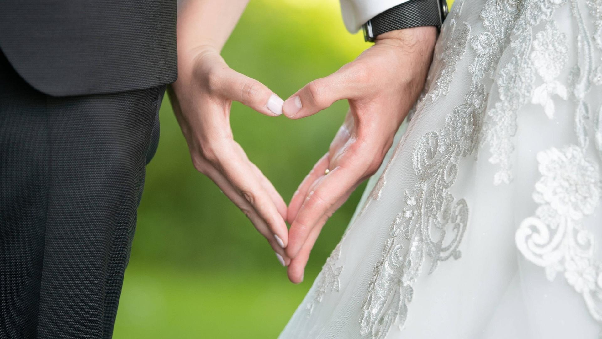 Ein Hochzeitspaar bildet mit seinen Händen ein Herz. | IMAGO, Silas Stein