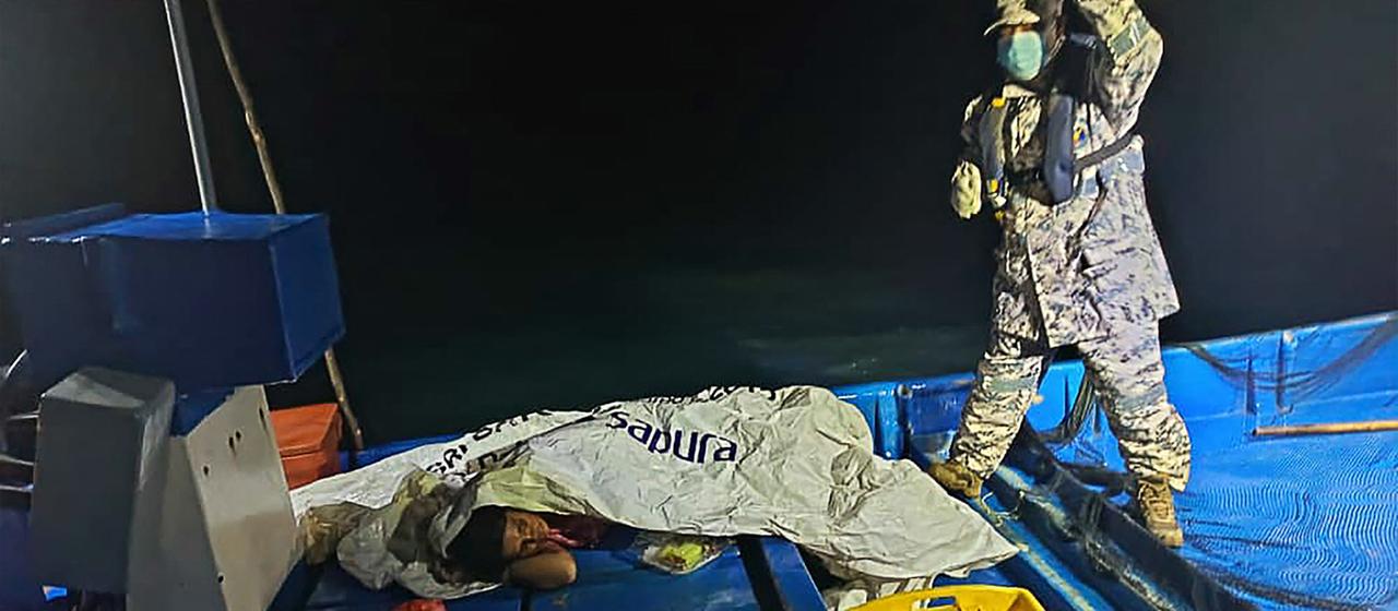 Ein Mitglied der malayischen Küstenwache mit Überlebenden eines Bootsunglücks.