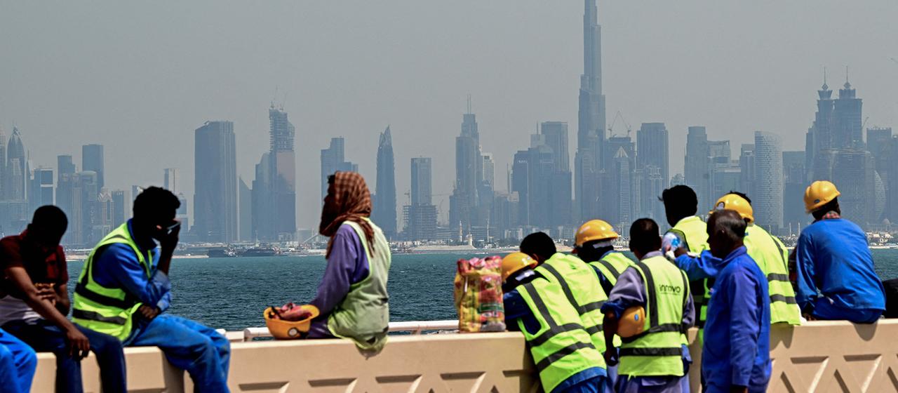 Arbeiter sitzen vor der Skyline der Stadt Dubai auf einer Mauer.