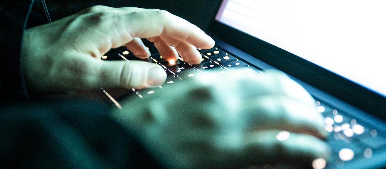 Eine Person tippt mit den Fingern auf einer beleuchteten Laptop-Tastatur.