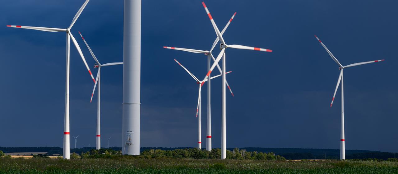 Mehrere Windkraftanlagen stehen sind vor dunklen Wolken zu sehen.