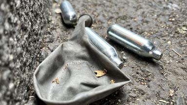 Mehrere Lachgaskartuschen und ein leerer Luftballon liegen auf einer Straße in London.