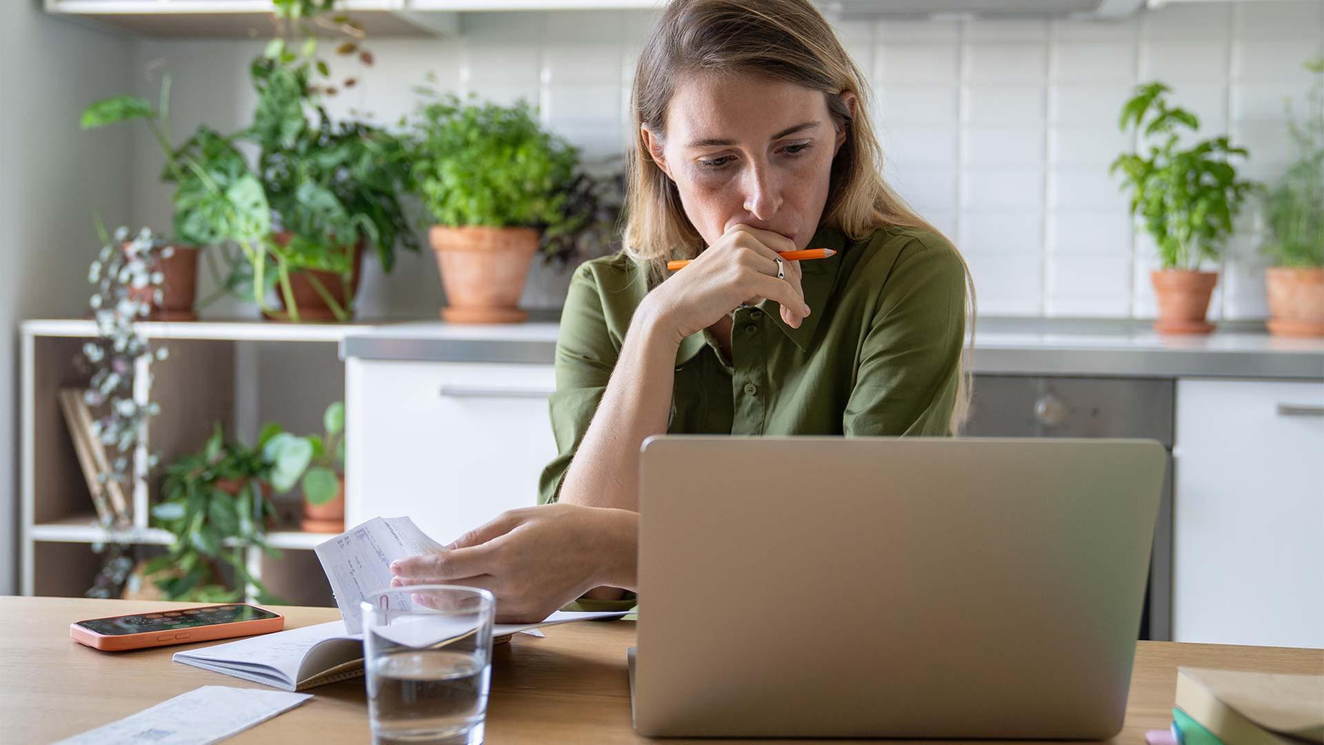 Eine Frau überprüft Ihre Finanzen und blickt konzentriert auf einen Laptop. | picture alliance / Zoonar