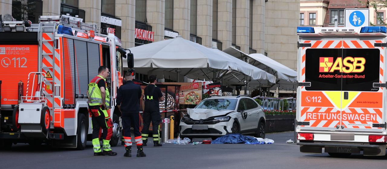 Rettungskräfte stehen in der Nähe eines beschädigten Autos an der Stelle, wo ein Auto in eine Menschengruppe gefahren ist.