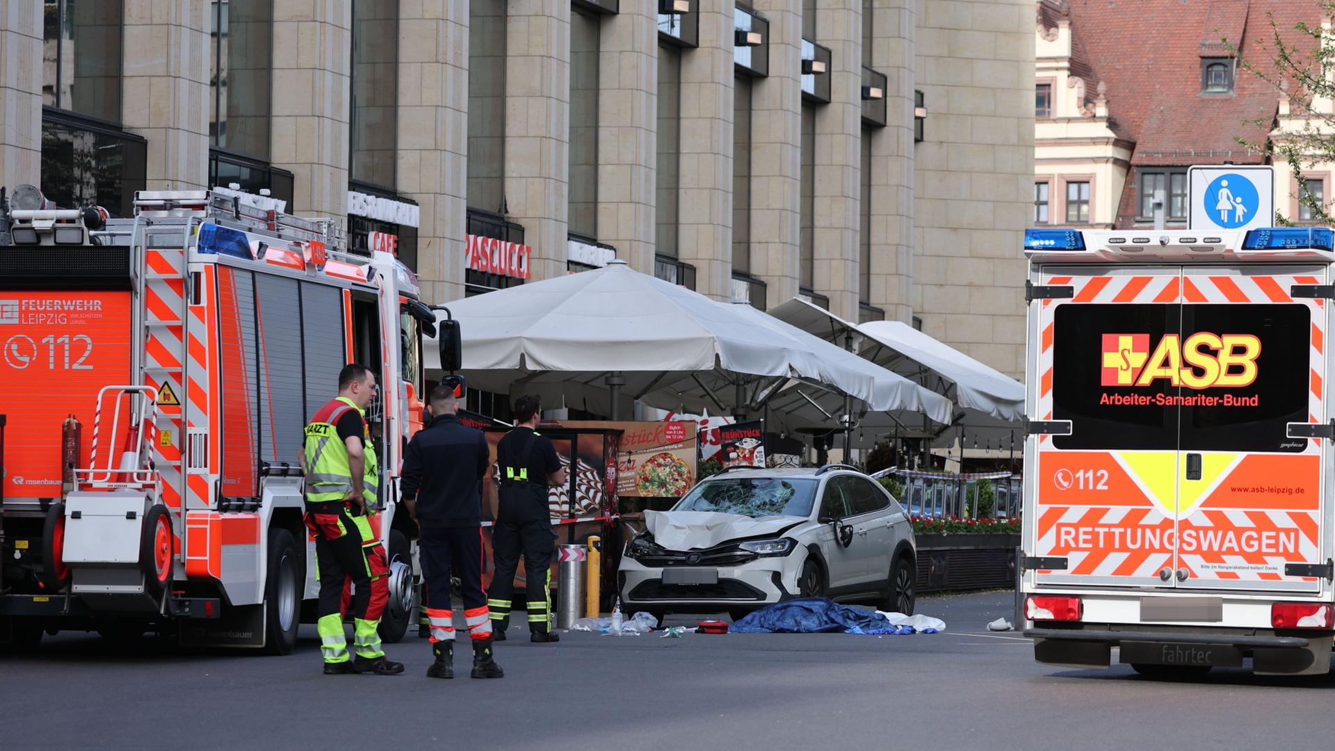 Rettungskräfte stehen in der Nähe eines beschädigten Autos an der Stelle, wo ein Auto in eine Menschengruppe gefahren ist. | Jan Woitas/dpa