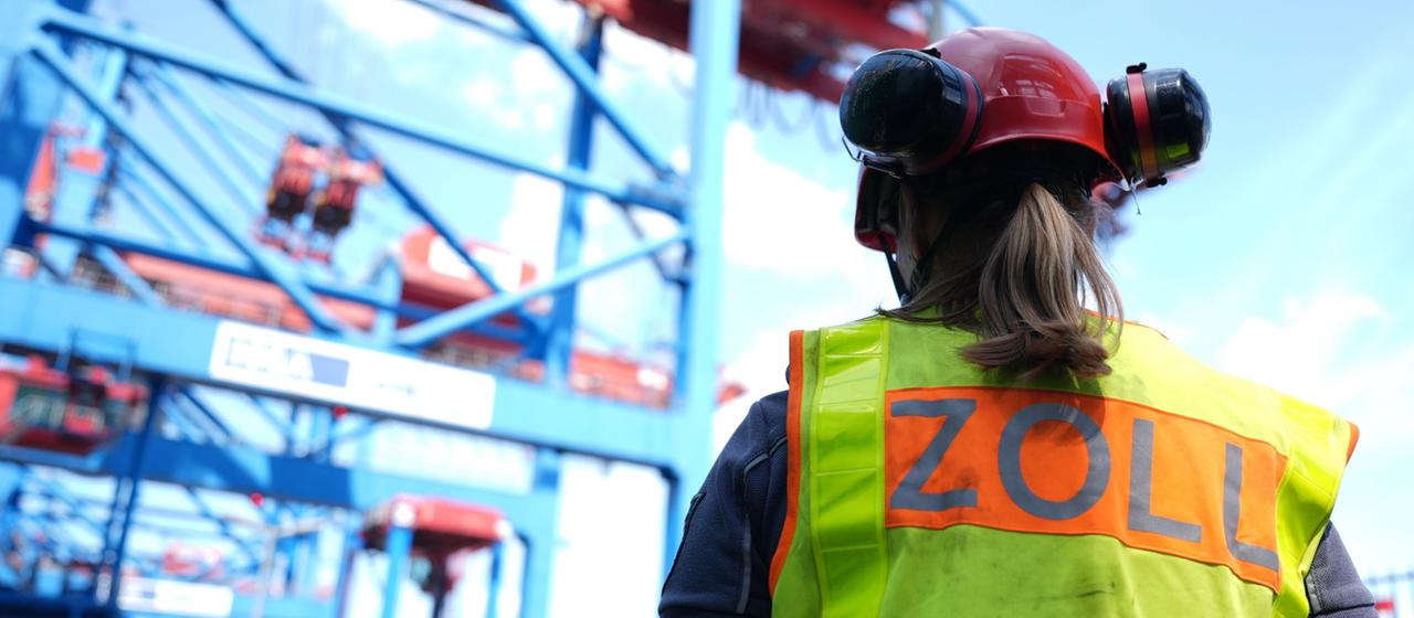Eine Zollbeamtin steht vor einem Containerschiff während einer Zollkontrolle. 