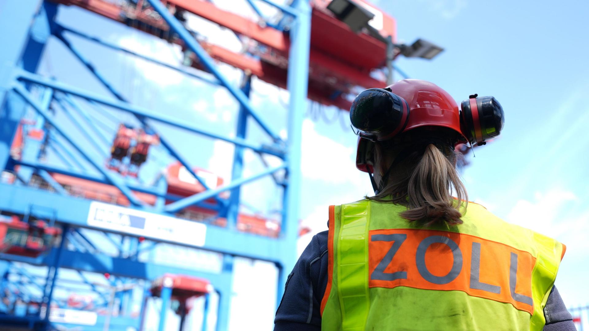 Eine Zollbeamtin steht vor einem Containerschiff während einer Zollkontrolle.  | Marcus Brandt/dpa