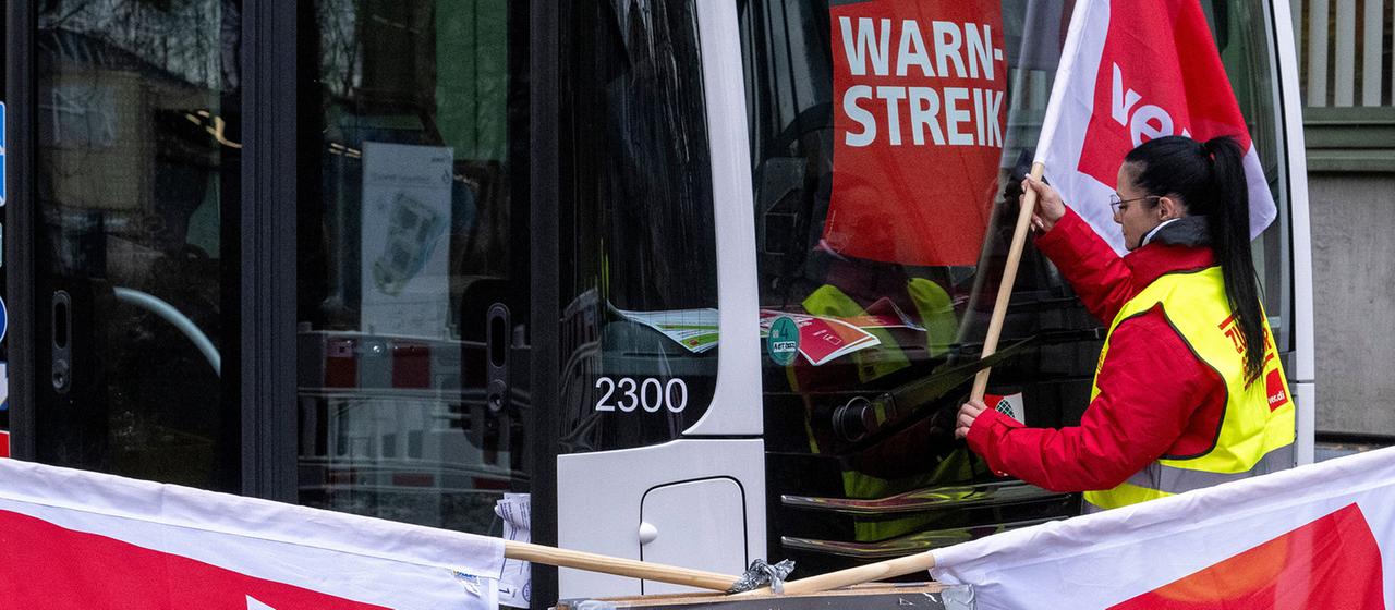  Eine Frau hängt eine Fahne der Gewerkschaft Verdi neben einen Warnstreikhinweis.