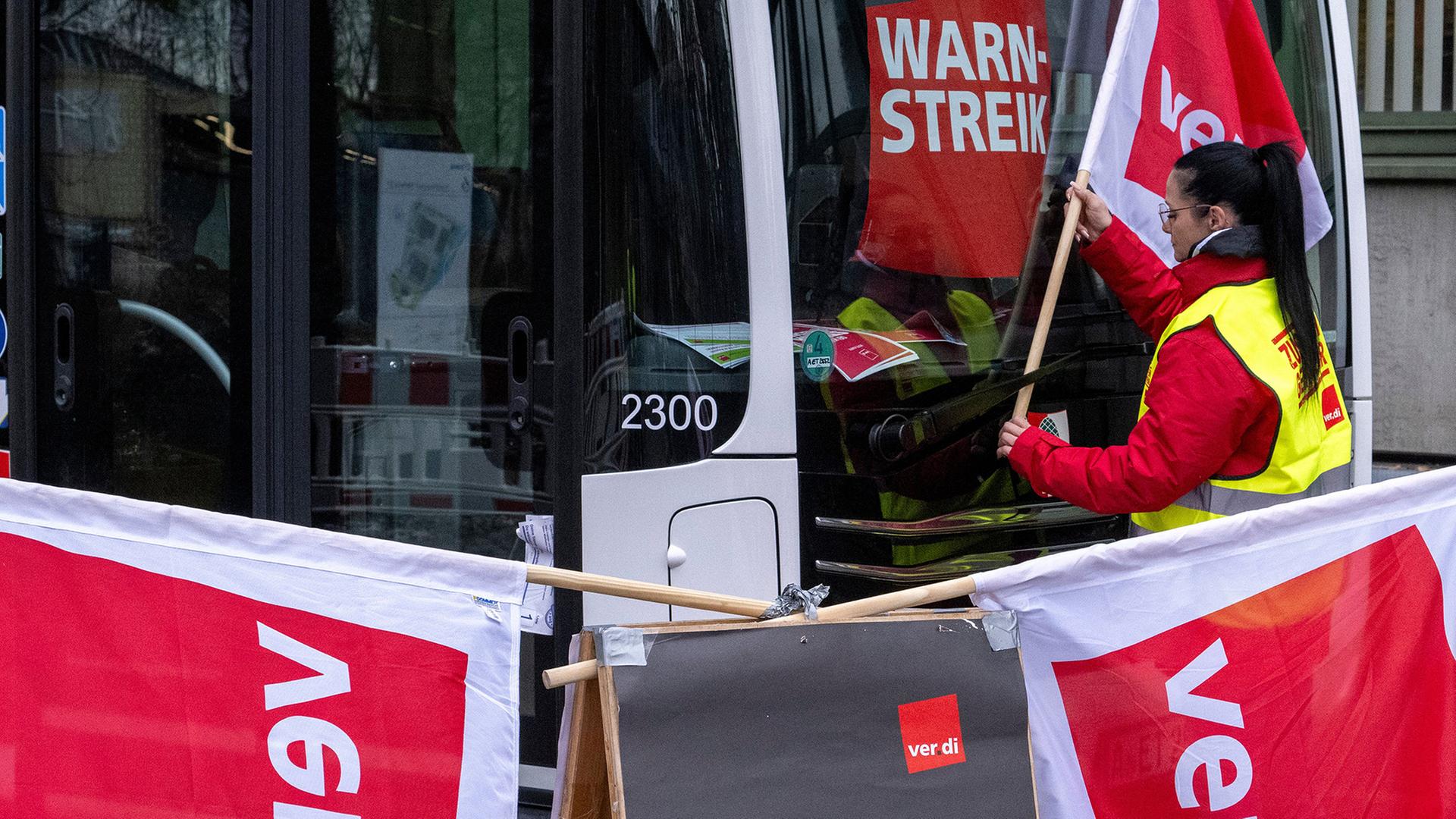  Eine Frau hängt eine Fahne der Gewerkschaft Verdi neben einen Warnstreikhinweis. | Stefan Puchner/dpa