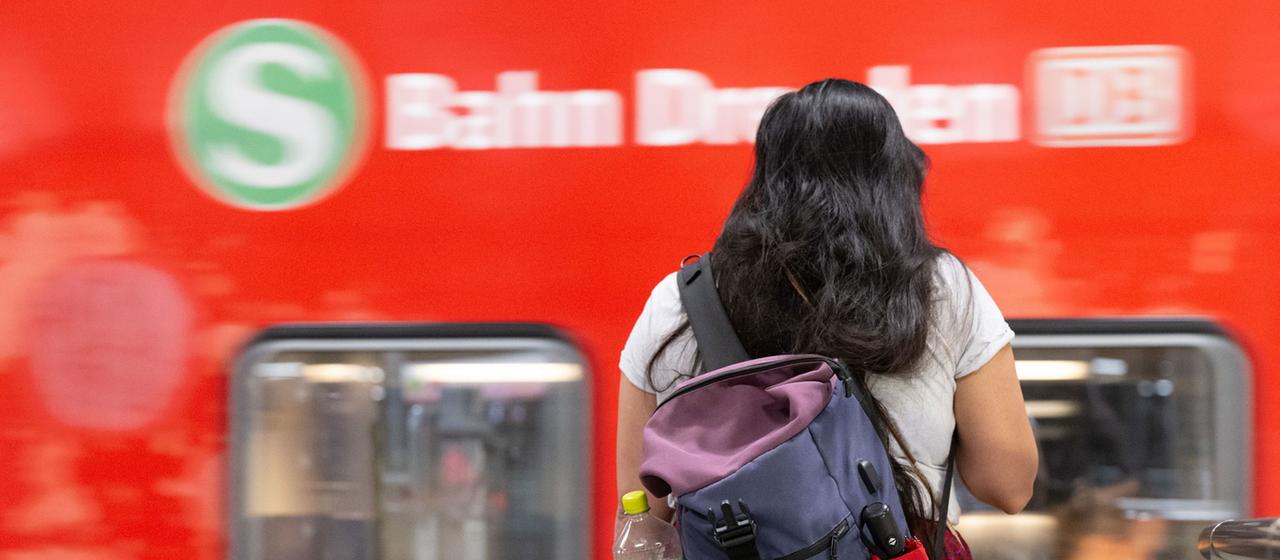 Eine Frau steht auf einem Bahnsteig vor einer S-Bahn.
