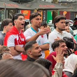 Drei junge Männer stehen zwischen weiteren Fußballfans und schauen das WM-Spiel 