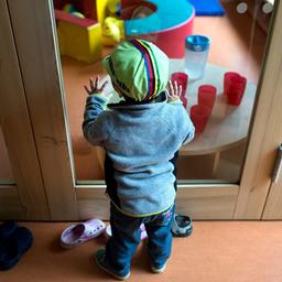 Ein Kind steht in einer Kindertagesstätte an einer Glasscheibe