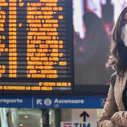 Eine Frau mit Atemschutzmaske steht vor einer Anzeigetafel am Bahnhof in Rom.