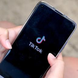 Ein Mädchen hält ein Smartphone in den Händen, auf dem das Logo der Kurzvideo-App TikTok zu sehen ist.