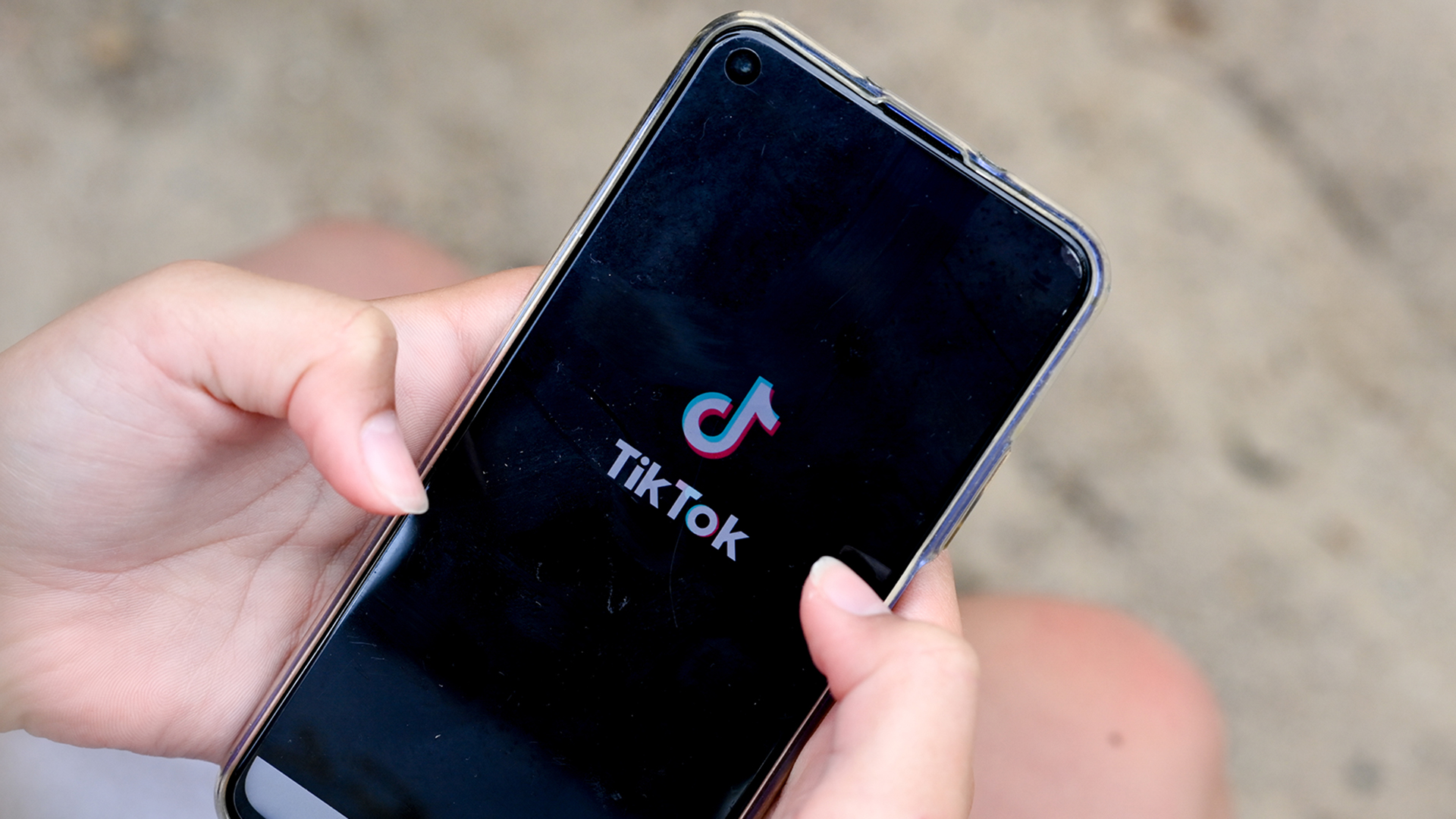 Ein Mädchen hält ein Smartphone in den Händen, auf dem das Logo der Kurzvideo-App TikTok zu sehen ist.