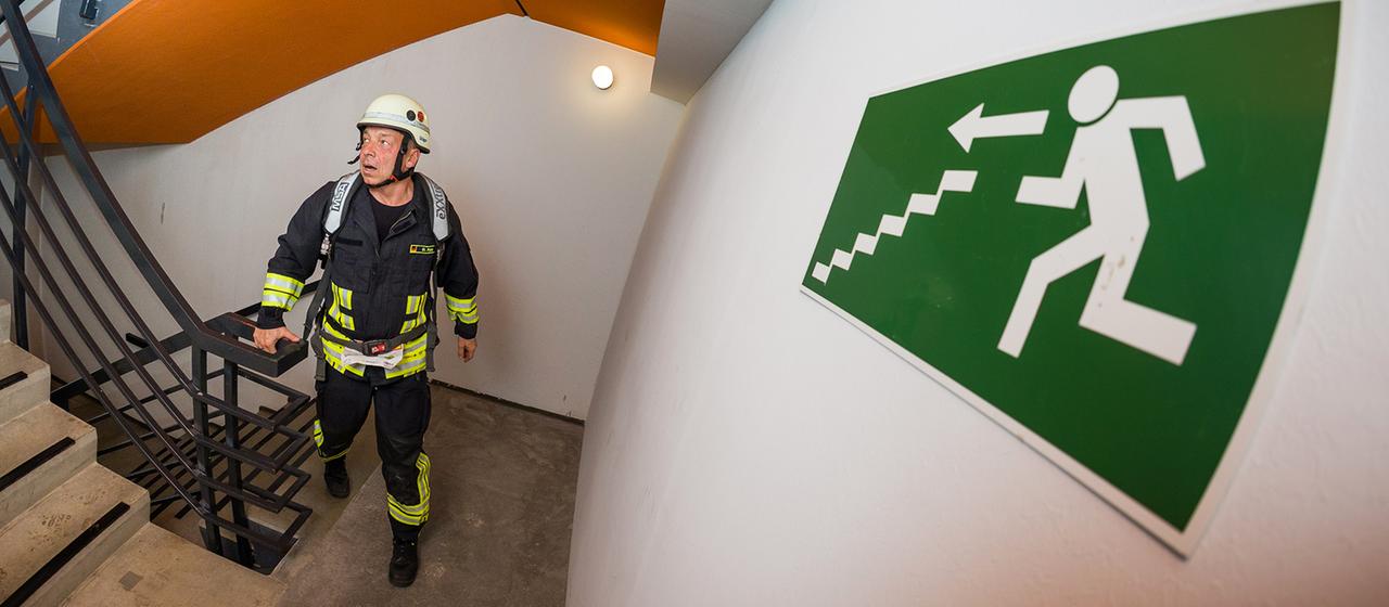  Ein Feuerwehrmann läuft in einem Treppen an einem Notausgangsschild vorbei.