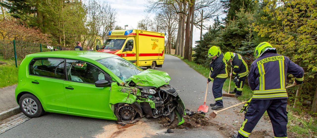 Drei Feuerwehrleute kehren die Reste eines Unfallwagens zusammen. | IMAGO/Andre März Drei Feuerwehrleute kehren die Reste eines Unfallwagens zusammen.