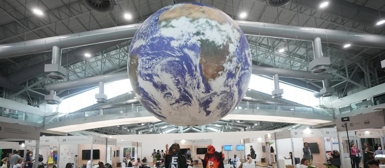 Aktivisten stehen unter einem Erdball, der von der Decke hängt.